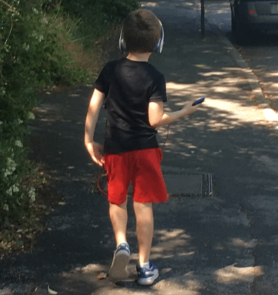 Photo of young boy walking and listening to music through headphones