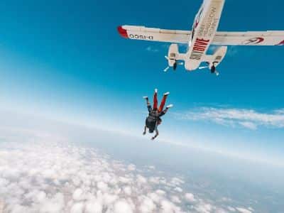 Photo of two people tandem skydiving out of a plane above the clouds