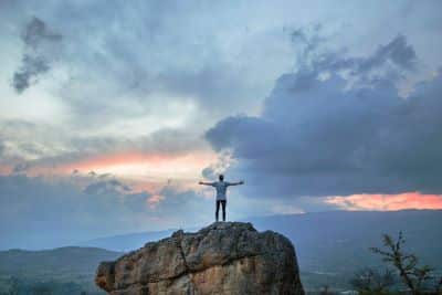 Photo of a man stood on a hilltop with his arms wide open