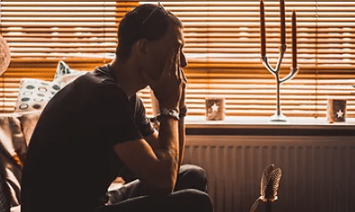 Photo of a man sat on a sofa with his hands holding his face