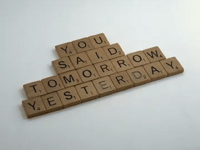 Photo of Scrabble game pieces on a white surface, ordered so they spell out 'You said tomorrow yesterday'.
